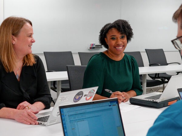 Photo of three people with laptops meeting at a table